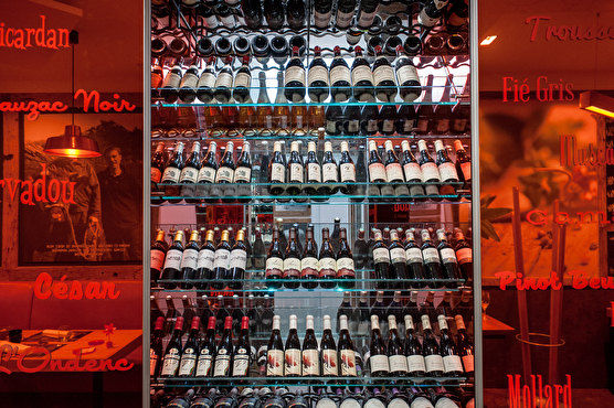Les bouteilles de vin sont rangées sur une structure moderne orange et vitrée. Sur le côté il est possible de lire des noms de vin.