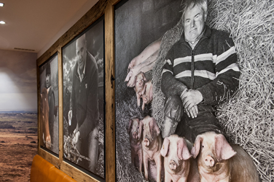 Un mur est décoré par des photographies d'agriculteurs avec leurs bêtes. Les agriculteurs sont en noir et blanc et les animaux sont en couleur.