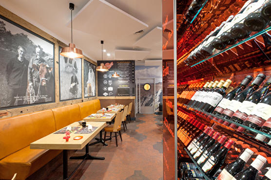 Derrière certaines tables de la salle de restaurant sont exposées des bouteilles de vin sur un mur moderne orange.