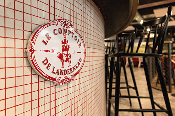 Sous le comptoir du bar se trouve le logo du restaurant en rouge et blanc.