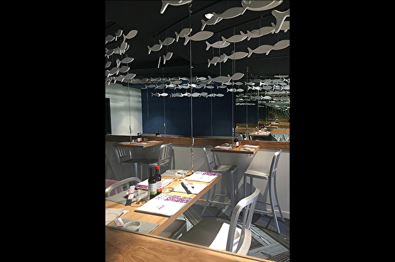 Un long miroir situé au-dessus des tables sur tout un pan de mur offre un effet de profondeur à la salle du restaurant. Des poissons suspendus au plafond décorent la salle.