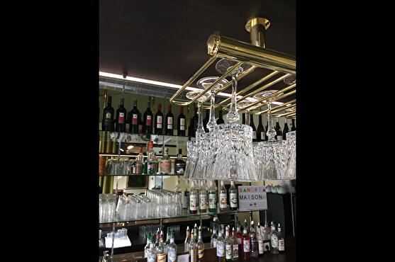 Derrière le comptoir du bar se trouvent des bouteilles qui couvrent le mur. Les verres à pied sont suspendus au-dessus du comptoir sur des structures dorées.