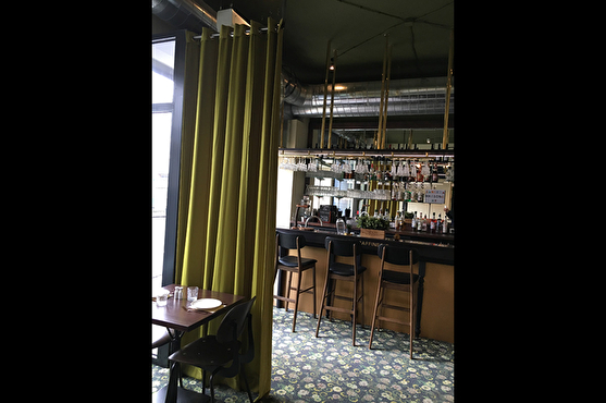 La Raffinerie au style contemporain possède un bar vintage, une moquette à motif floral et des chaises anciennes. La salle de restaurant et le bar sont séparés par un grand rideau vert.