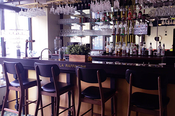 Le bar au style contemporain possède un bar design en bois. Il est surplombé par des verres à pied suspendus par leur pied.