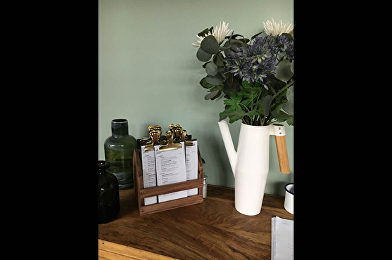 Sur une des tables en bois, sur laquelle on peut retrouver la carte vintage du restaurant, se trouvent un vase avec des fleurs et d'autres vases vides.